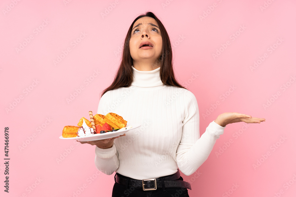 Young brunette woman holding waffles over isolated pink background frustrated by a bad situation Young brunette woman holding waffles over isolated pink background frustrated by a bad situation