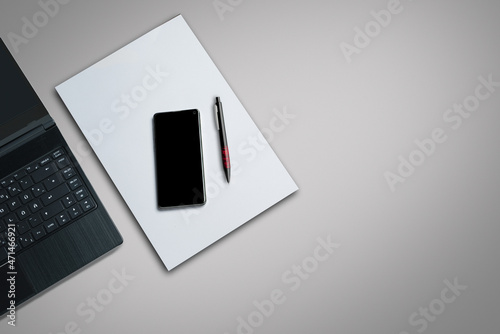 laptop on a desk with smartphone,  white paper and pen
