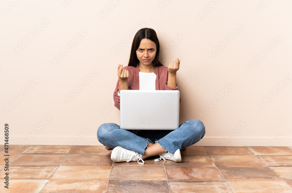 Young mixed race woman with a laptop sitting on the floor making money gesture but is ruined Young mixed race woman with a laptop sitting on the floor making money gesture but is ruined