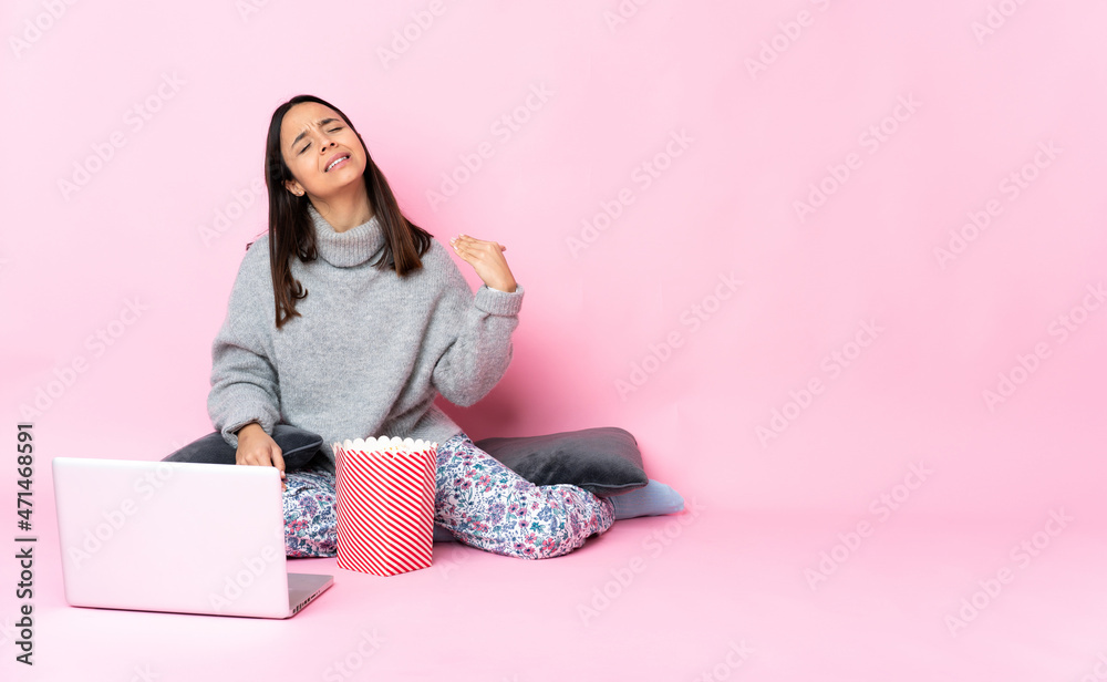 Young mixed race woman eating popcorn while watching a movie on the laptop with tired and sick expression Young mixed race woman eating popcorn while watching a movie on the laptop with tired and sick expression