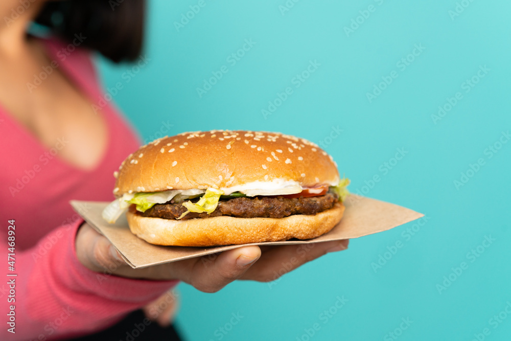 Young brunette woman holding a burger over isolated background