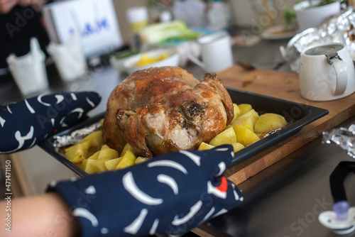 Woman preparing whole roasted chicken with baked potatoes in the home kitchen