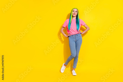 Photo of dreamy adorable young vibrant woman wear pink t-shirt looking empty space arms waist isolated yellow color background