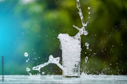 Drink water pouring in to glass over sunlight and natural green background.Water splash in glass. glass of water in green garden blurred background.