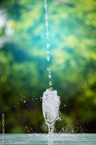 Drink water pouring in to glass over sunlight and natural green background.Water splash in glass. glass of water in green garden blurred background.
