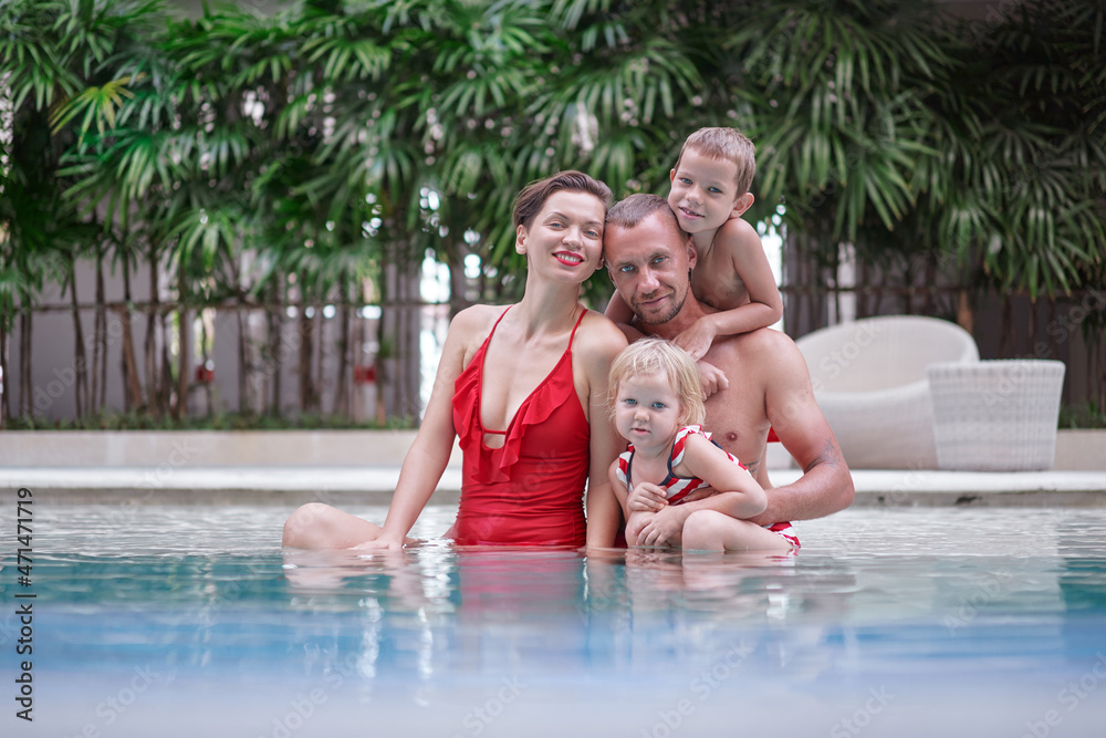 Fototapeta premium Vacation with a family. Happy young parents and their kids having fun in swimming pool.