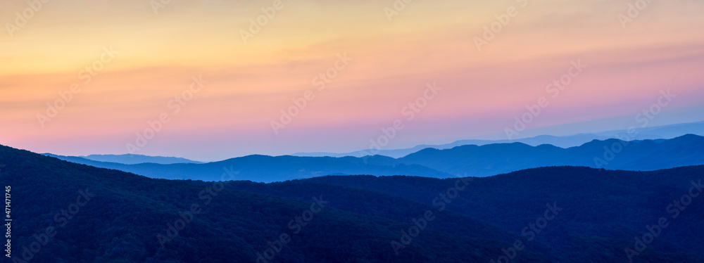 Yellow-orange sunset in the mountains above the hills. Panorama of a mountain landscape during the blue hour