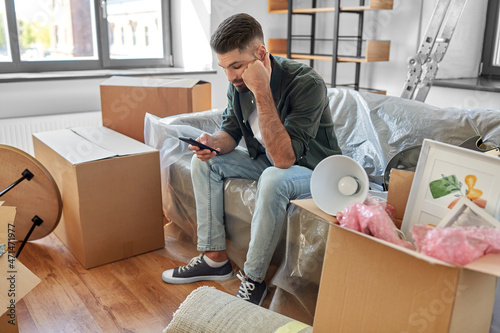 Tableau sur toile moving, eviction and real estate concept - sad man with smartphone and boxes at