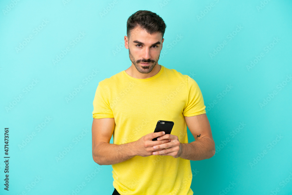 Young caucasian man isolated on blue background sending a message with the mobile Young caucasian man isolated on blue background sending a message with the mobile
