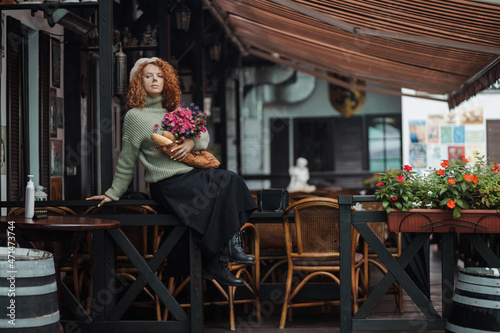 A woman in a beret and a green sweater holds a bouquet of flowers on a restaurant background