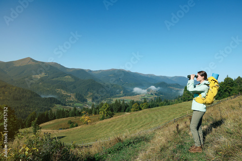 Tourist with hiking equipment looking through binoculars in mountains