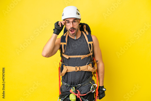 Young caucasian rock climber man isolated on yellow background with glasses and surprised