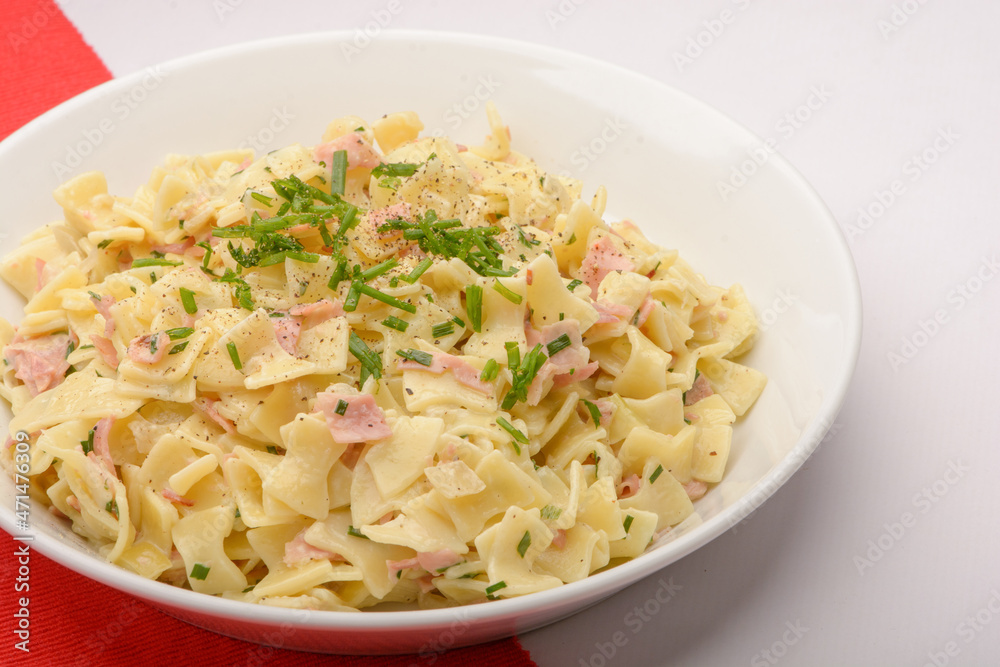 Traditional Austrian Dish so called Schinkenfleckerl on a white plate with red and white background Traditional Austrian Dish so called Schinkenfleckerl on a white plate with red and white background