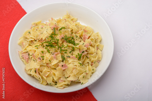 Traditional Austrian Dish so called Schinkenfleckerl on a white plate with red and white background