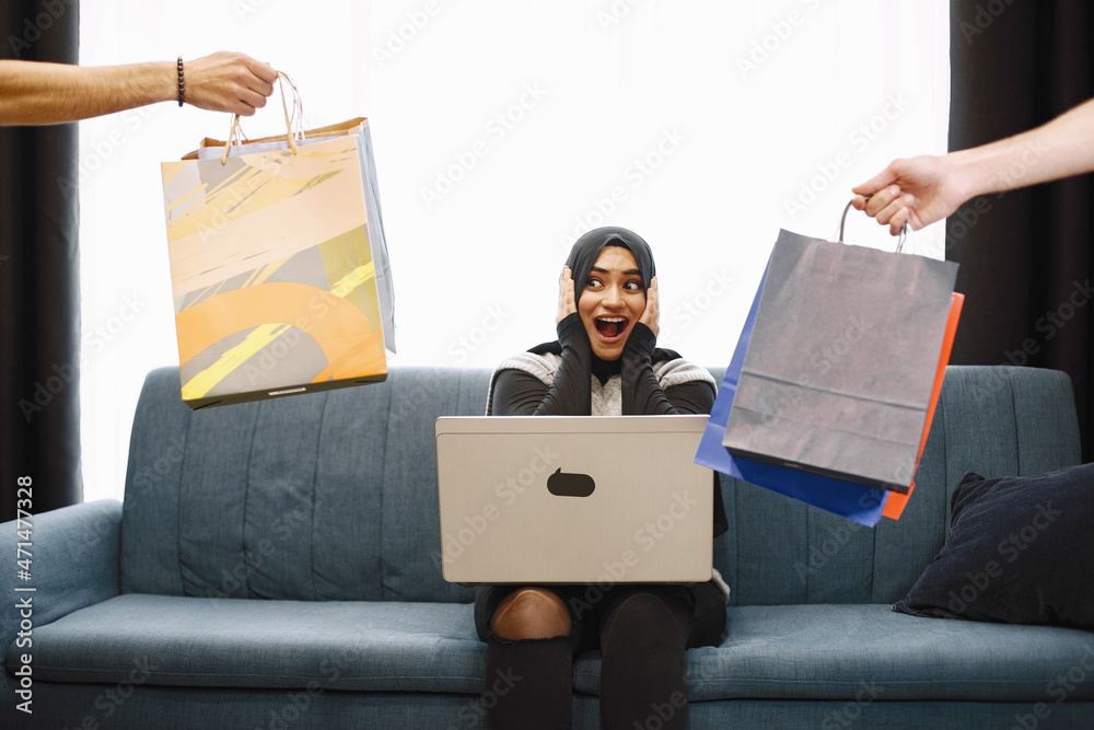 Arabic woman in headscarf using laptop at home, doing shopping online Arabic woman in headscarf using laptop at home, doing shopping online