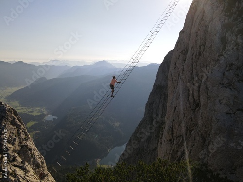 One of the most famous via ferratas in the world. The Intersport via ferrata on Donnerkogel in Austria. A man climbs to the other side of the mountain using a ladder