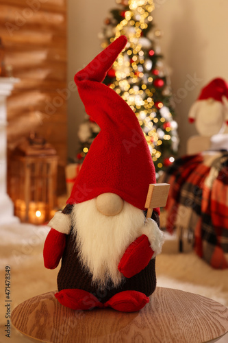 Cute Christmas gnome on wooden table in room with festive decorations