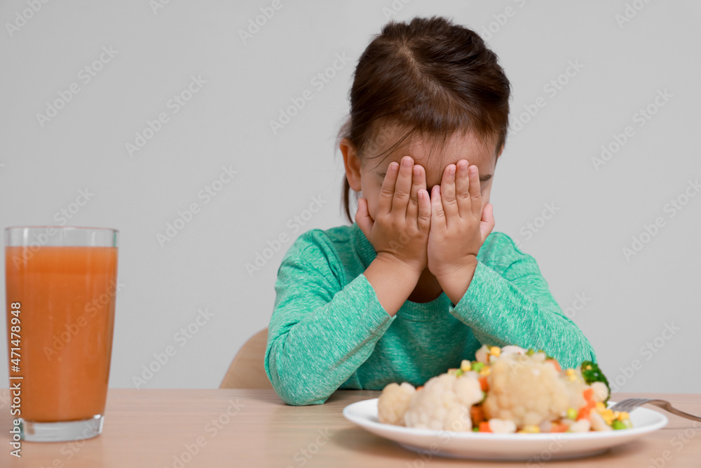 Cute little girl crying and refusing to eat vegetable salad at table on grey background Cute little girl crying and refusing to eat vegetable salad at table on grey background