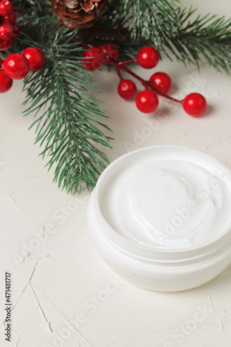 Jar with moisturizing face cream on the background of fir branches and berries of viburnum. Top view. Natural winter cosmetic for skin care.