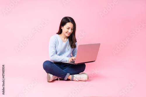 portrait of young asian girl sitting using laptop, isolated on pink background © 1112000
