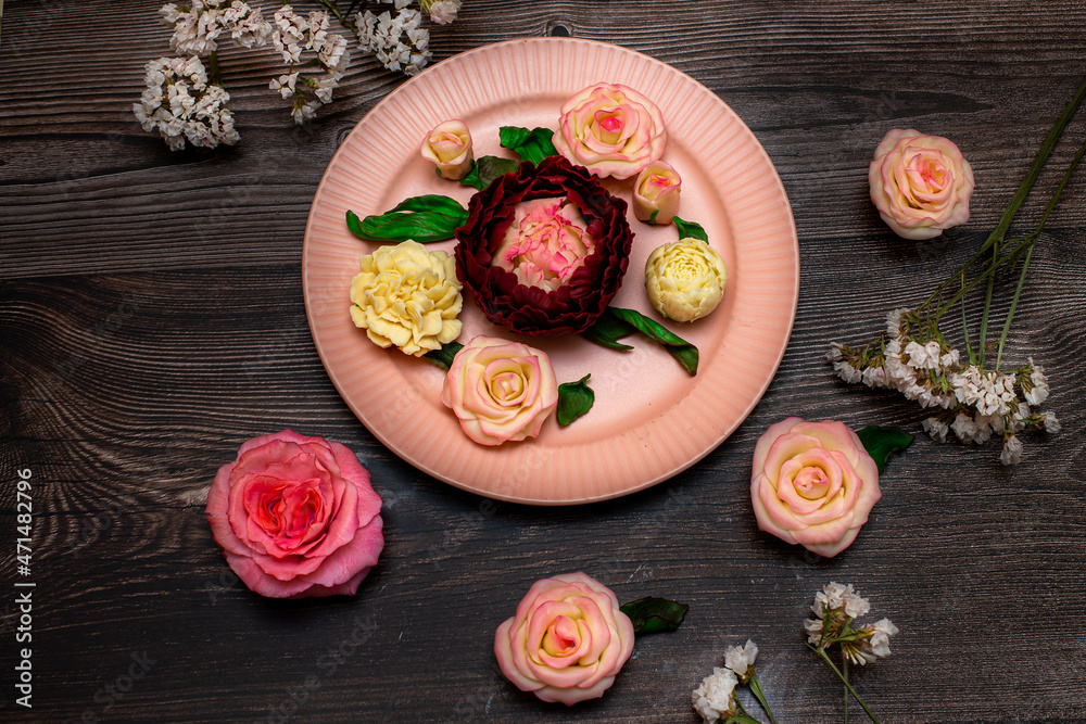 Chocolate pink roses, white roses, peonies are in the pink plate on a background of dark wood.