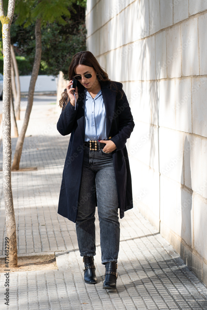 Mujer bonita de negocios hablando por teléfono mientras pasea por la calle