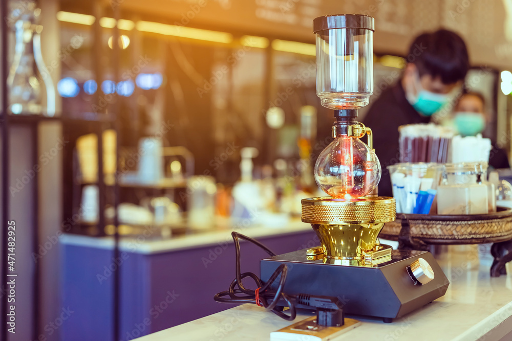 Close up to barista make coffee with Vacuum Pot Syphon Brewer.  Syphon (Siphon) coffee maker brews drink using two chambers where vapor pressure and vacuum produce coffee in cafe. Selective focus.
