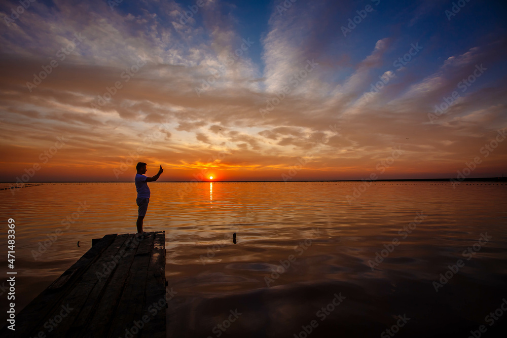 a man takes a photo on the phone of a pink salt lake at sunset. Ukraine