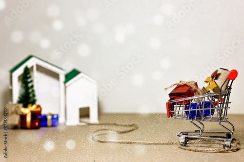 Merry Christmas, Happy New Year and Boxing day concept. Present boxes, shopping cart, pine tree and house models on light brown background. © Eve