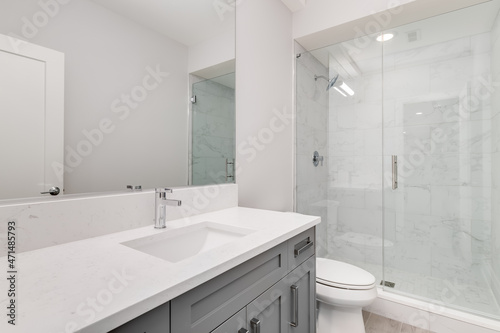 A white bathroom with a grey vanity and a white marble stand up shower.