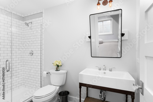 A luxurious modern farmhouse bathroom with a tilting mirror  pedestal sink  and a subway tiled white shower.