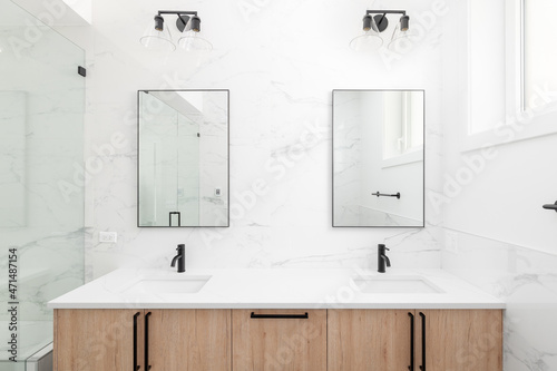 Fotobehang A beautiful renovated bathroom with a wood cabinet, white granite countertop, dual black mirrors, and the wall lined with marble