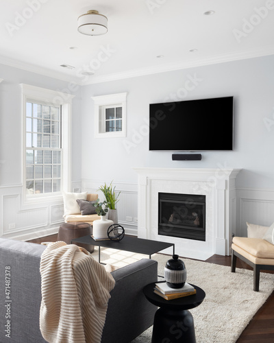 A cozy living room with seating set around a mounted television and white marble tiled fireplace.