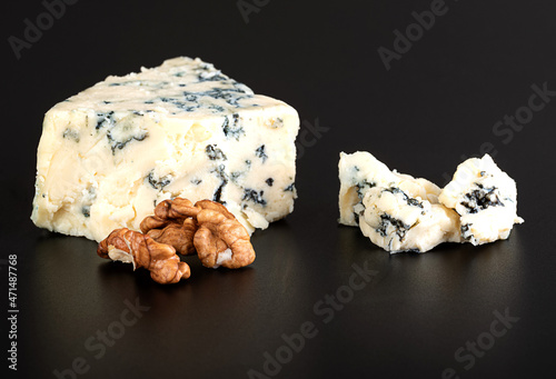 A piece of delicious aromatic cheese with blue mold (Gorgonzola, Roquefort, Stilton, Danablouin) with walnut on a glossy black background with reflection