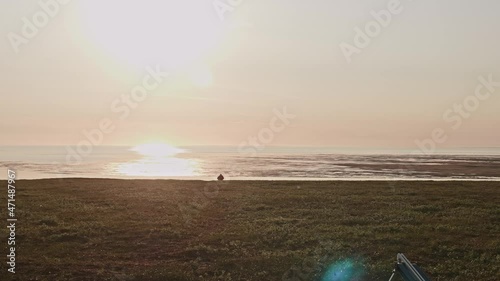 Backlit of man going to river shore and adrone starting its flight in the sky. Amazing sunset in the middle of Tundra in Russia photo