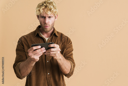White blonde man wearing shirt playing online game on cellphone © Drobot Dean
