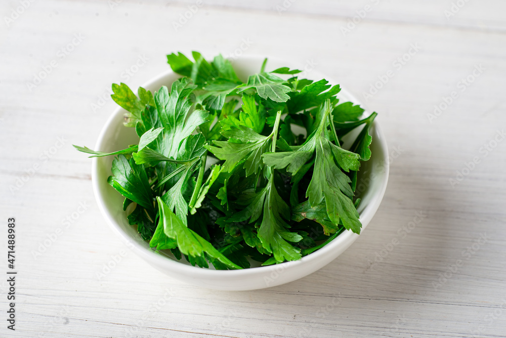 Fresh parsley on a plate on a white wooden background. Cooking ingredient. Fresh parsley on a plate on a white wooden background. Cooking ingredient.