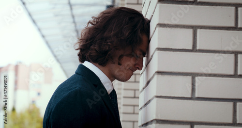 Angry nervous young businessman corporate worker banging his head against the wall in despair. Frustrated man entrepreneur looking worried about project loss.