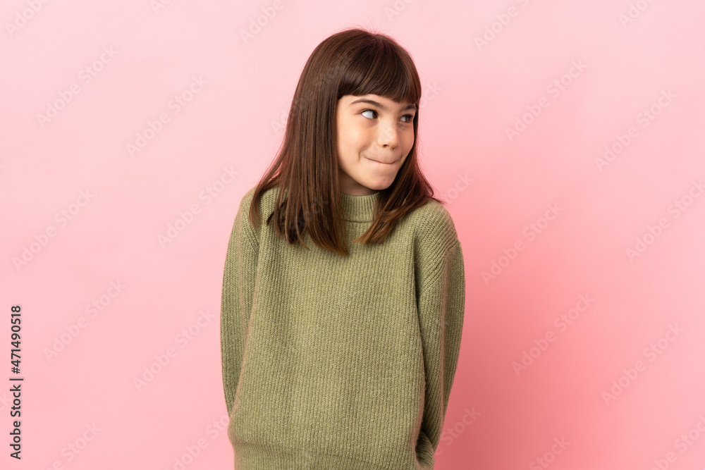 Fototapeta premium Little girl isolated on pink background having doubts while looking up