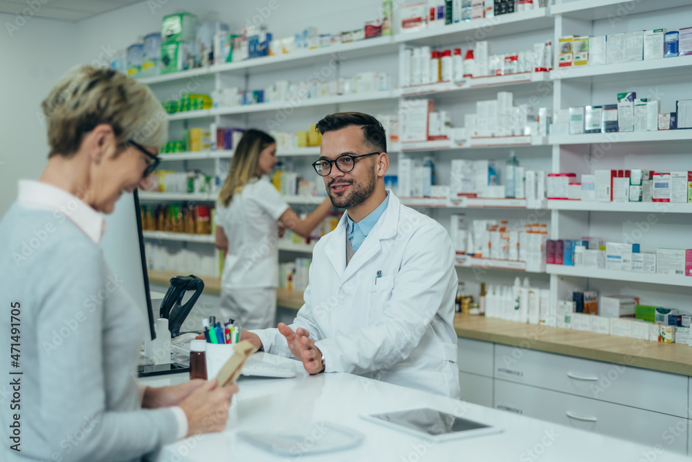 Male pharmacist selling medications at drugstore to a senior woman customer