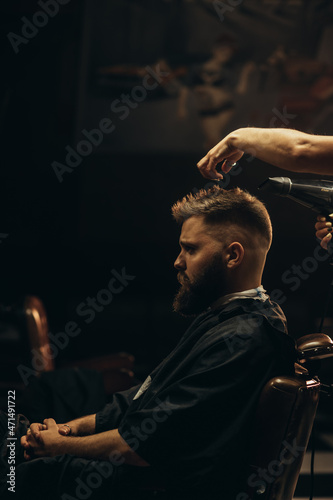 Fotografie Young bearded man getting haircut by hairdresser