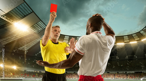 Football referee showing a player a red card for breaking rules at crowded stadium over night cloudy sky. photo