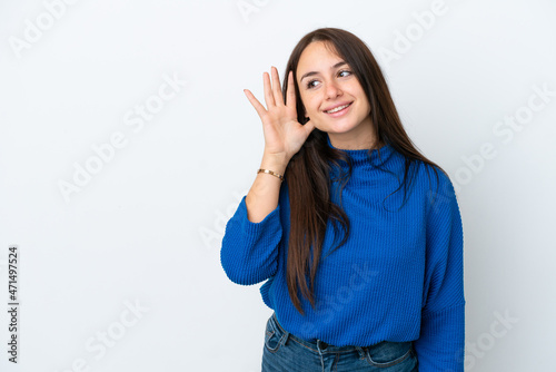 Young Ukrainian woman isolated on white background listening to something by putting hand on the ear