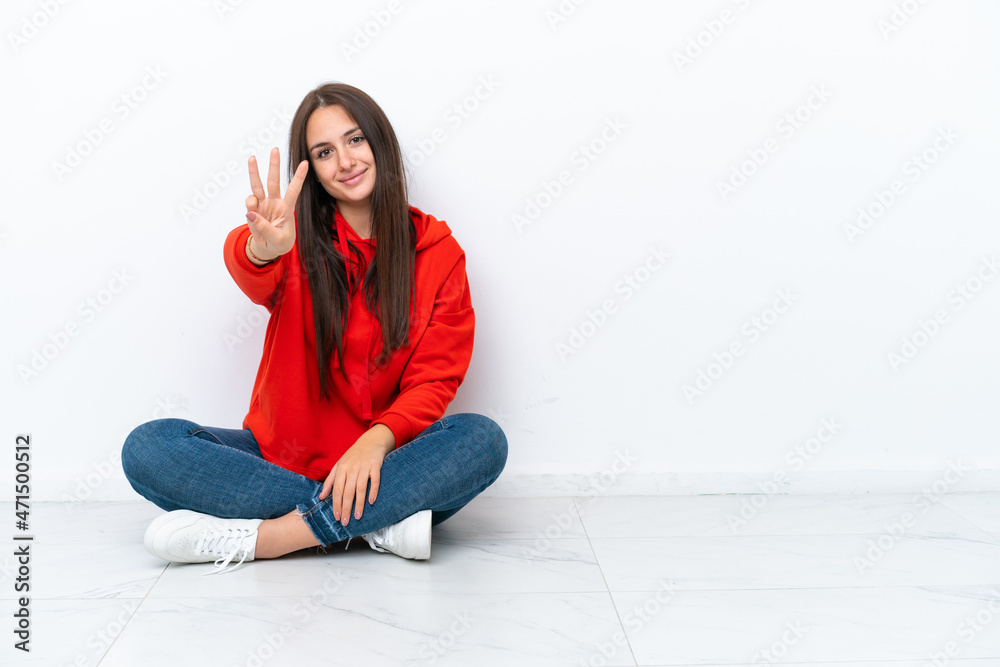 Young Ukrainian woman sitting on the floor isolated on white background happy and counting three with fingers Young Ukrainian woman sitting on the floor isolated on white background happy and counting three with fingers