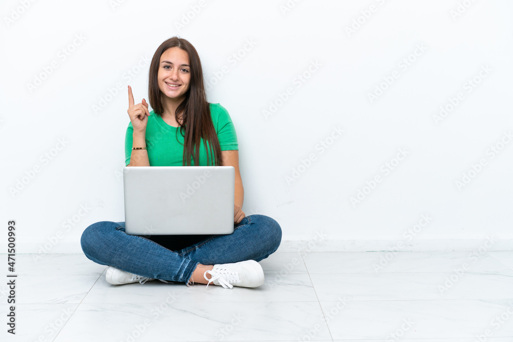 Young Ukrainian woman with a laptop sitting on floor showing and lifting a finger in sign of the best Young Ukrainian woman with a laptop sitting on floor showing and lifting a finger in sign of the best