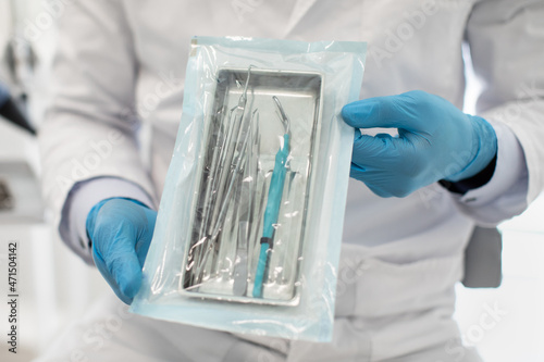 Doctor Wearing Blue Sterile Gloves Demonstating Sealed Sterilization Pouch With Dental Tools