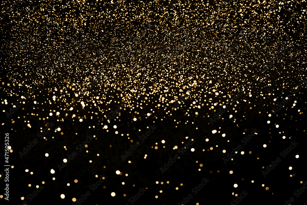 Black festive background. Abstract scattering of gold sparkles on black. Holiday backdrop, selective focus