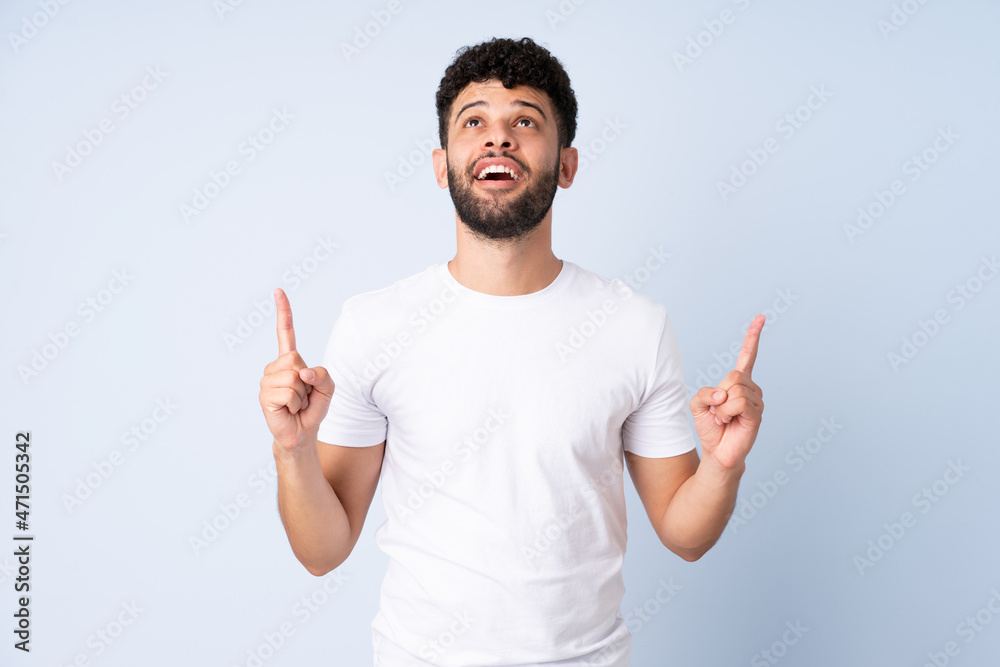 Young Moroccan man isolated on blue background surprised and pointing up Young Moroccan man isolated on blue background surprised and pointing up