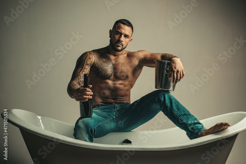 Sexy seductive muscular man sit on bathtub, men holiday with champagne. Celebrating christmas or birthday. Private sex party.
