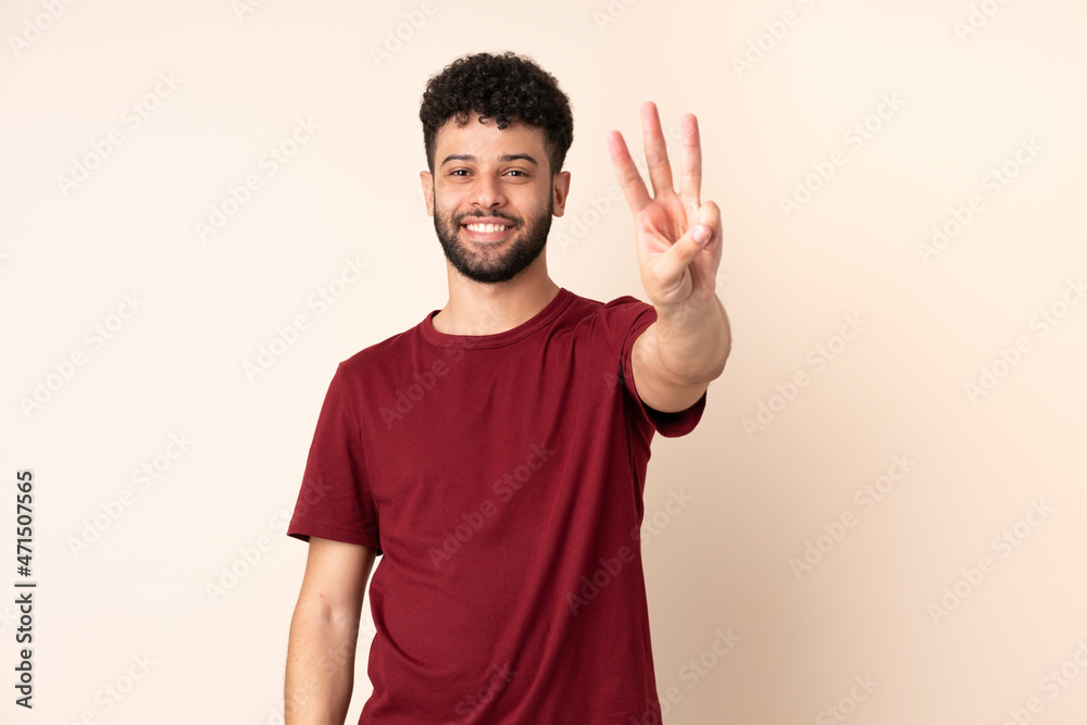 Young Moroccan man isolated on beige background happy and counting three with fingers Young Moroccan man isolated on beige background happy and counting three with fingers